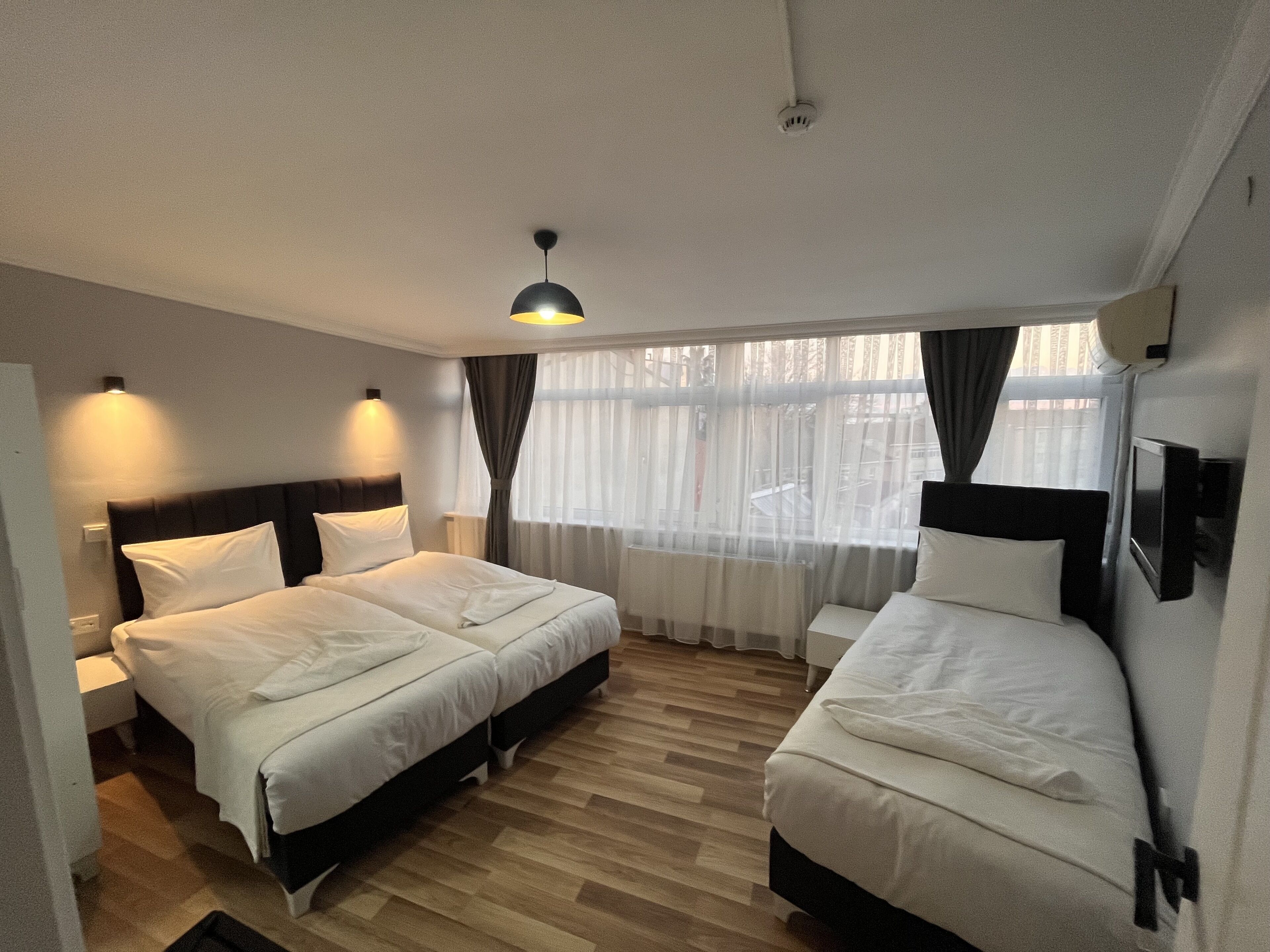 Camera d'albergo con due letti, una lampada a soffitto, una finestra con tende e una TV a parete.