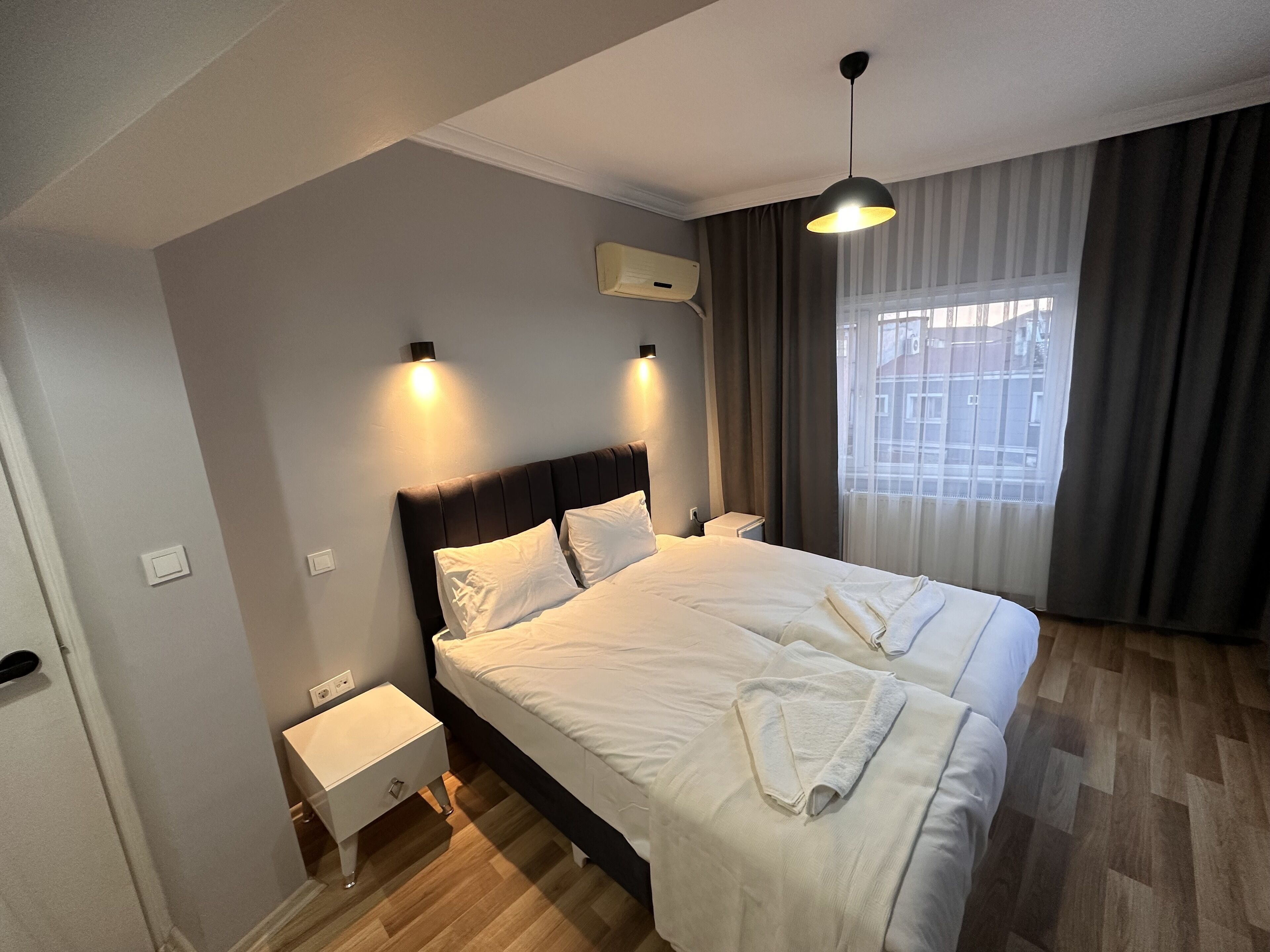 A hotel room with a large bed, bedside tables, a window with curtains, and a ceiling light.