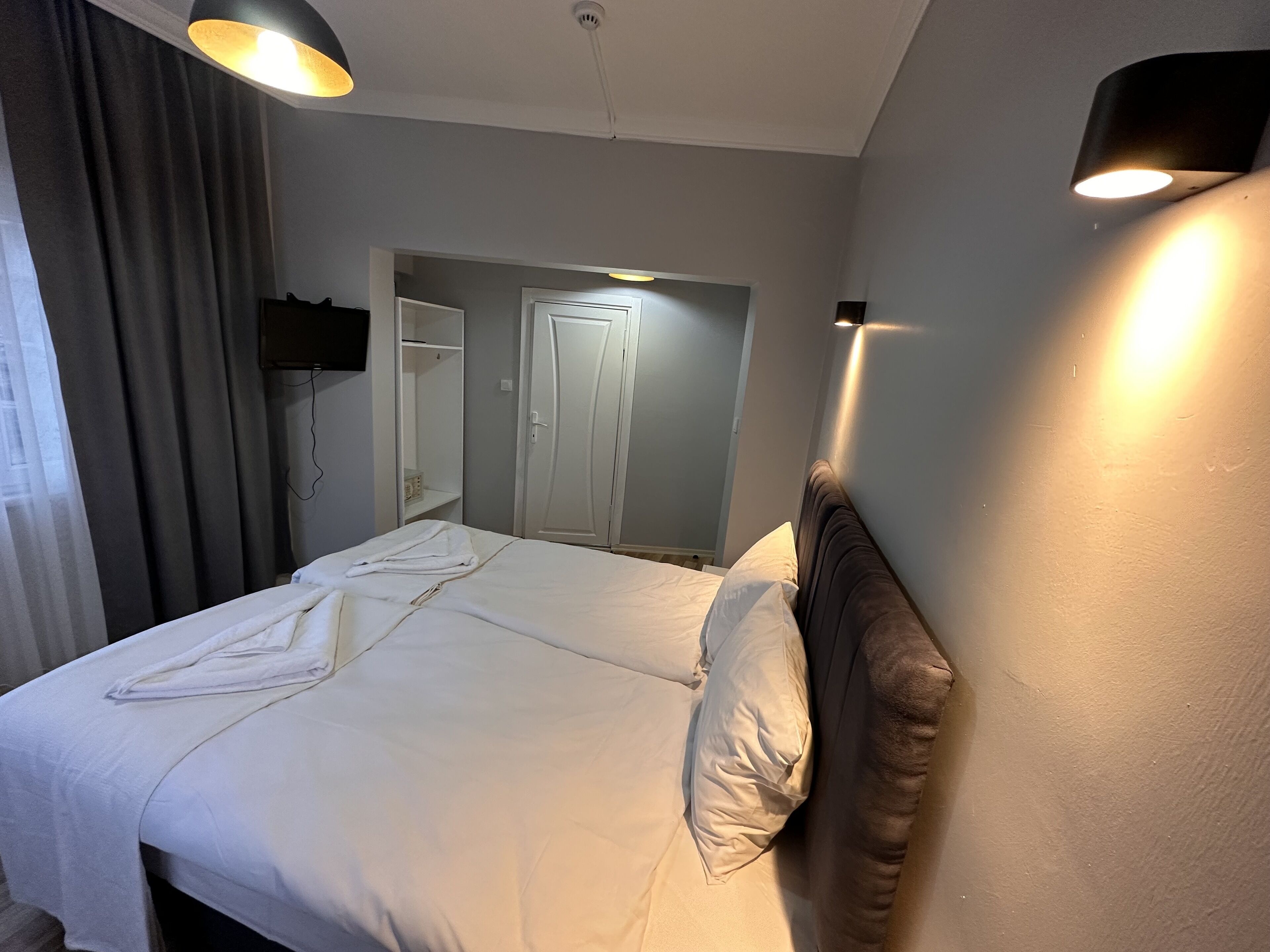 Una habitación de hotel con una cama, un televisor montado en la pared y una puerta que da a otra habitación.