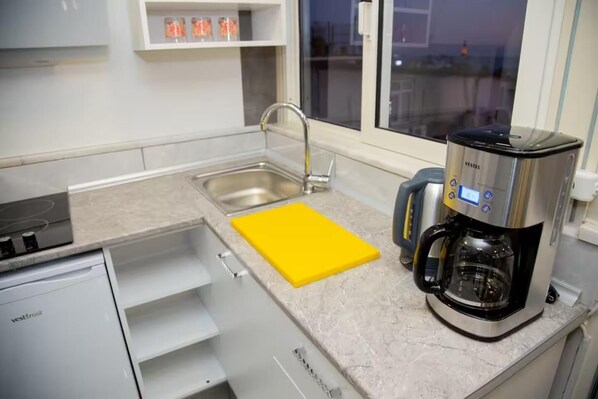 Una cocina moderna con una cafetera de acero inoxidable, una tabla de cortar amarilla y un lavamanos.