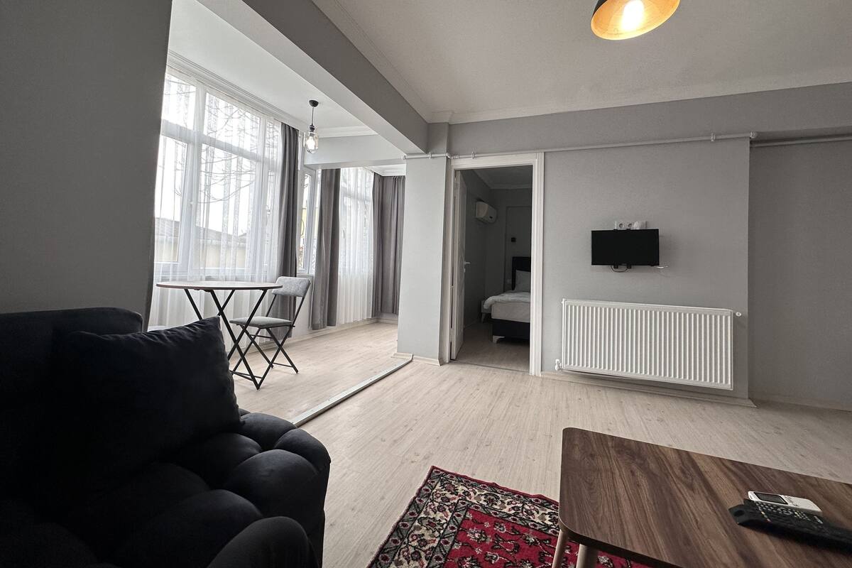 A modern living room with a sofa, a coffee table, a dining table with chairs, and a TV mounted on the wall.