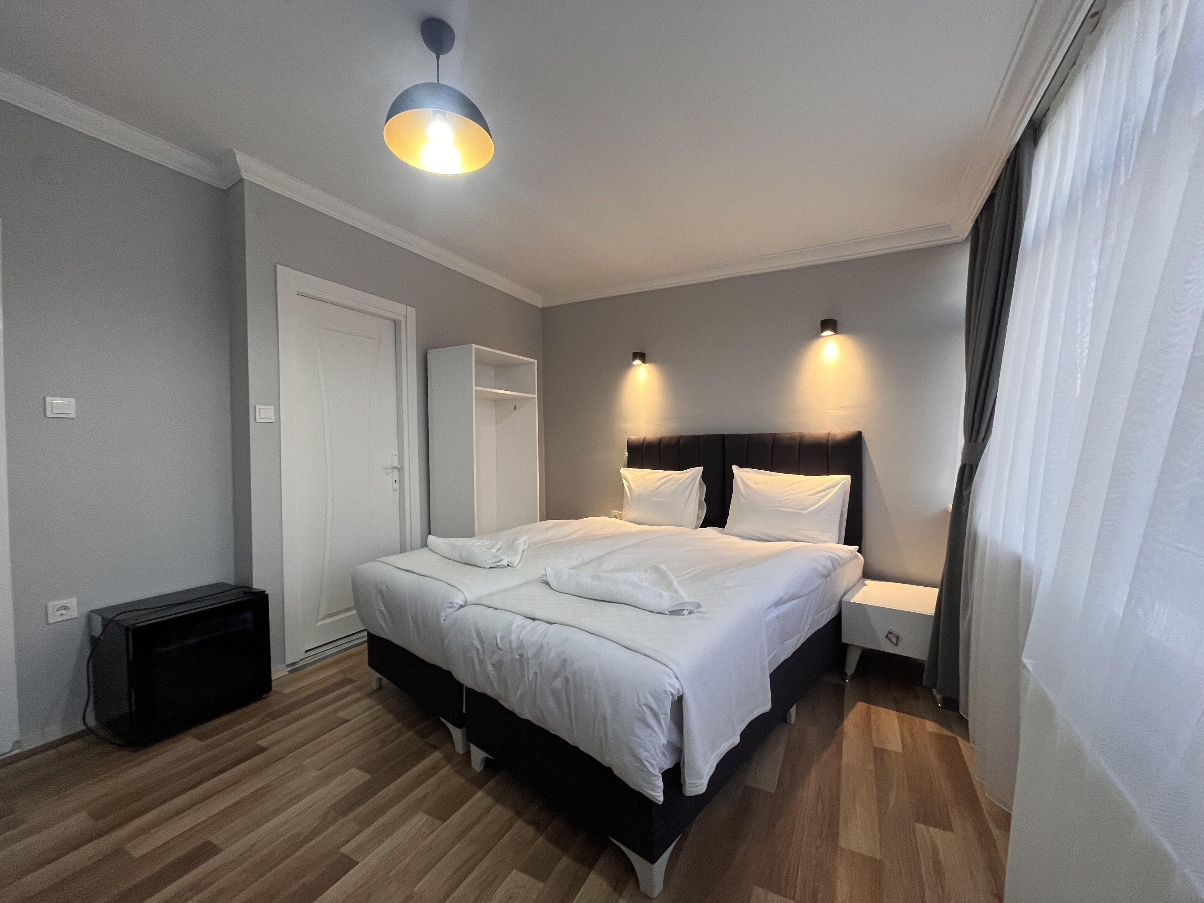 Un dormitorio ordenado con cama, mesitas de noche, armario y una lámpara en el techo.