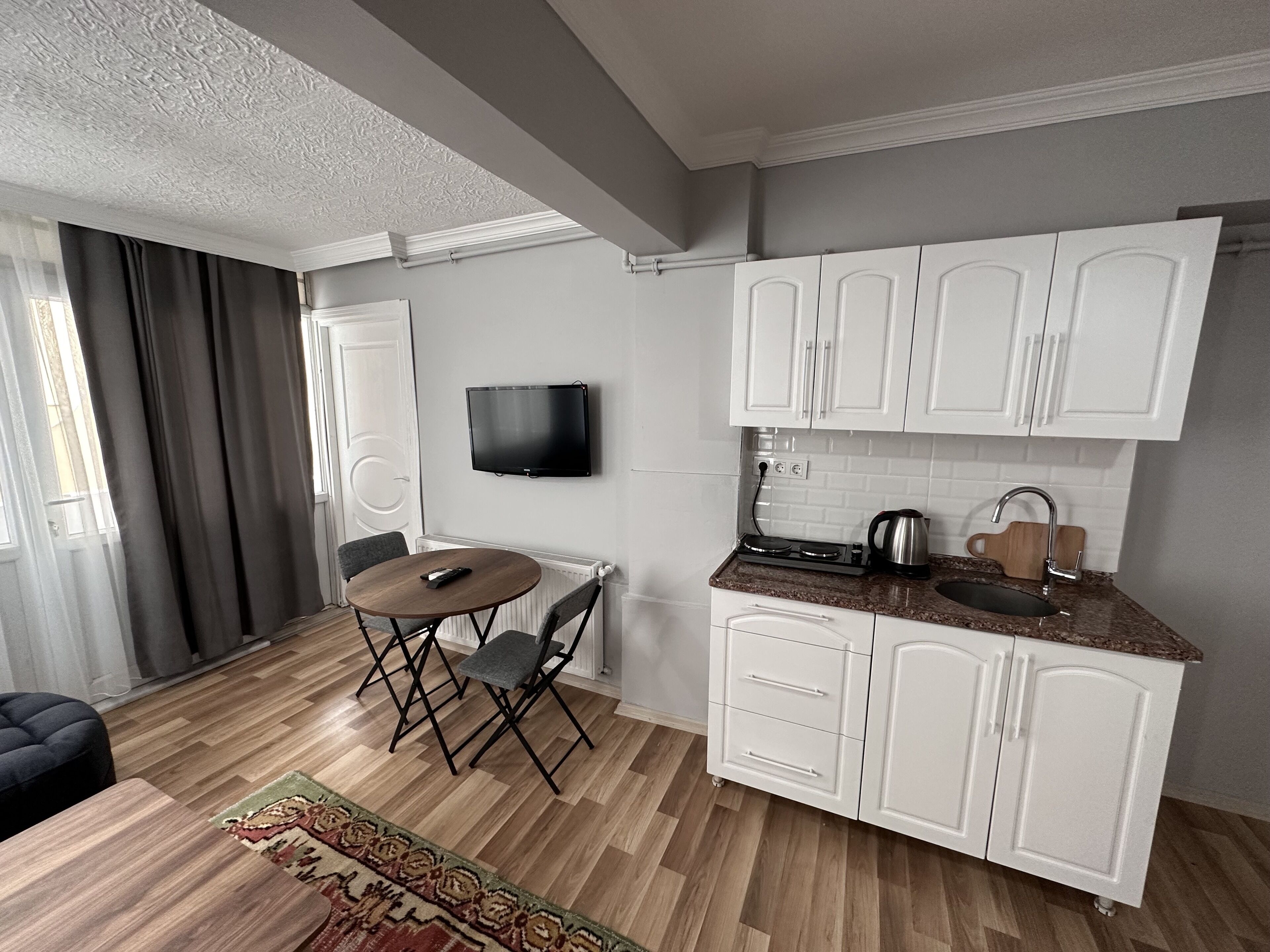 A compact kitchen with white cabinets, a built-in stove, and a flat-screen TV mounted on the wall.