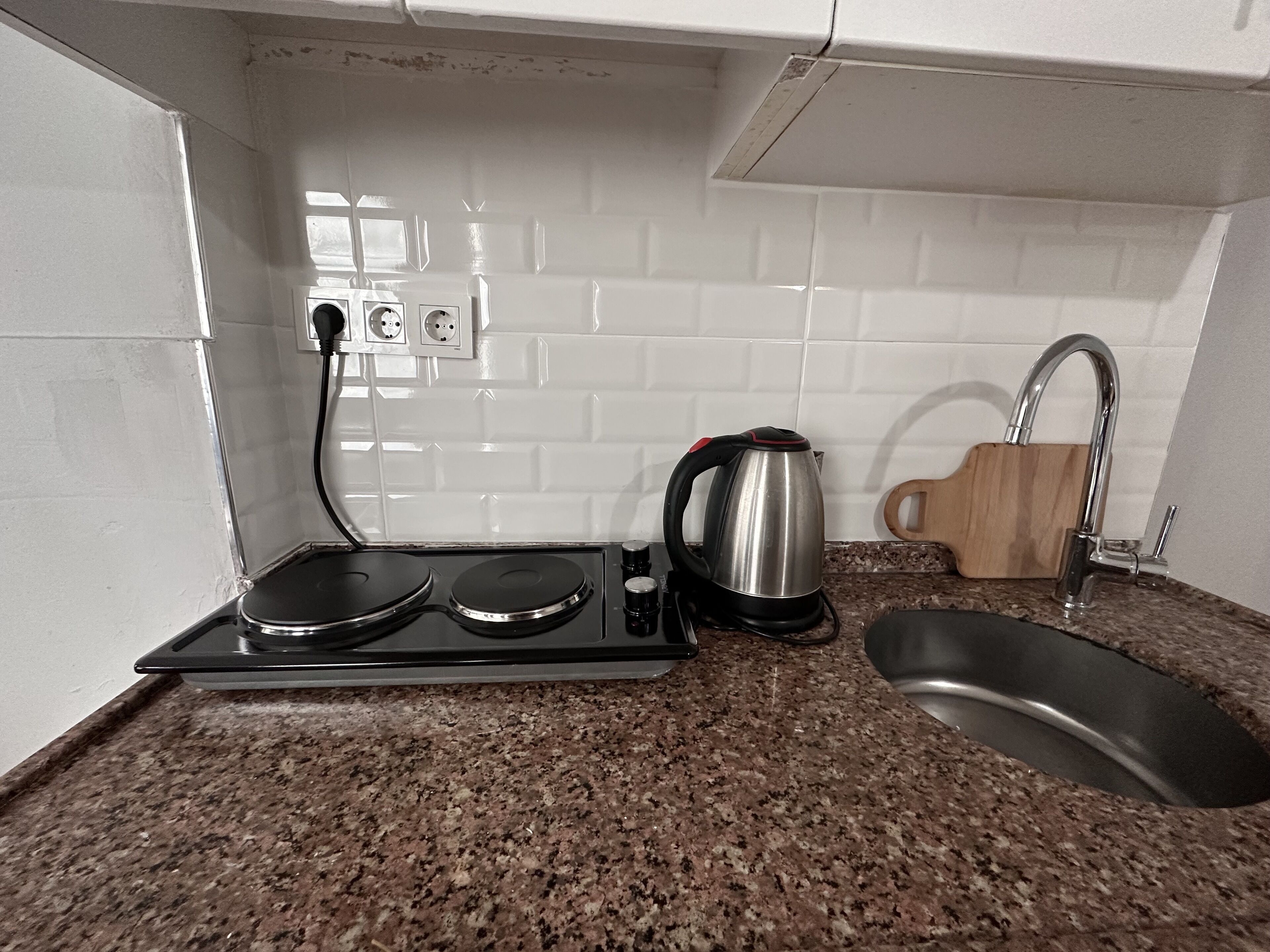 A kitchen with a granite countertop, a kettle, a sink, and a stove.