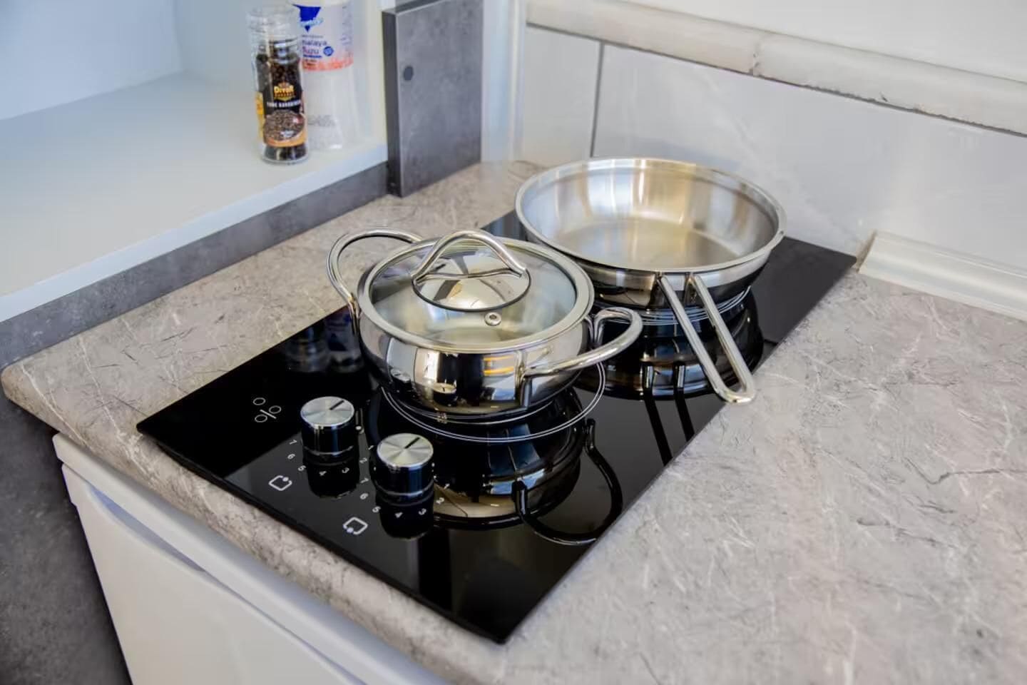 A kitchen with a black induction cooktop, two stainless steel pots, and a spice rack with bottles.
