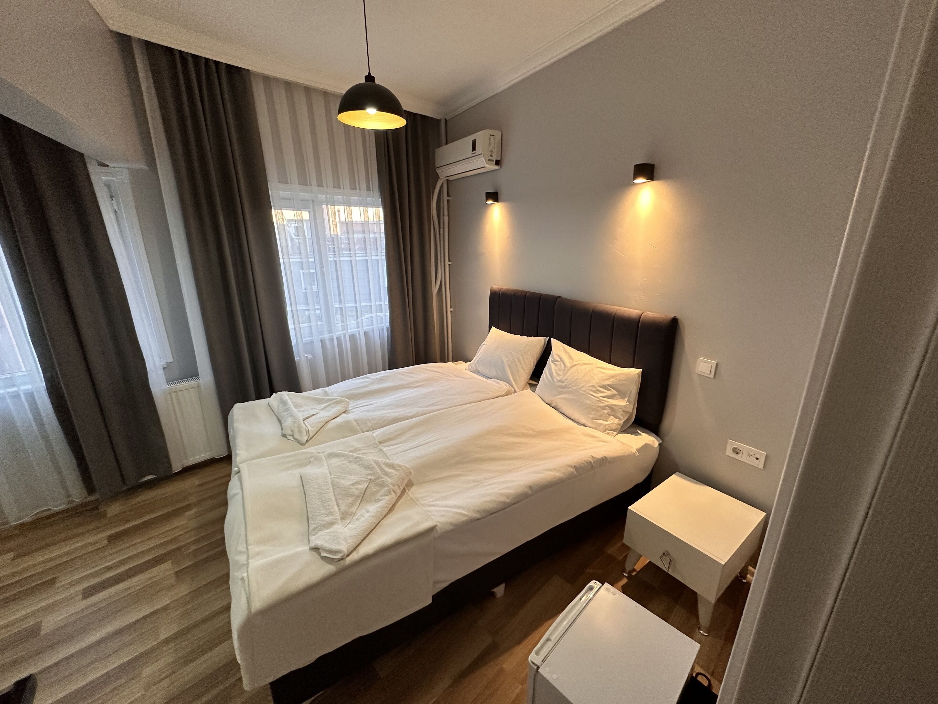 A neatly made bed with white linens, a dark headboard, and two bedside tables with lamps.