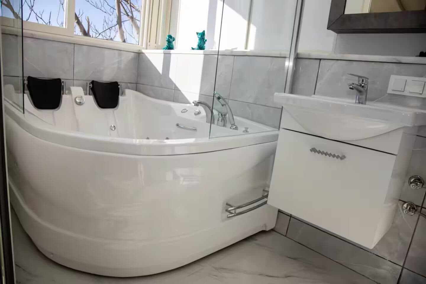 Un baño moderno con una bañera independiente, un tocador con lavabo y una ventana con adornos decorativos.