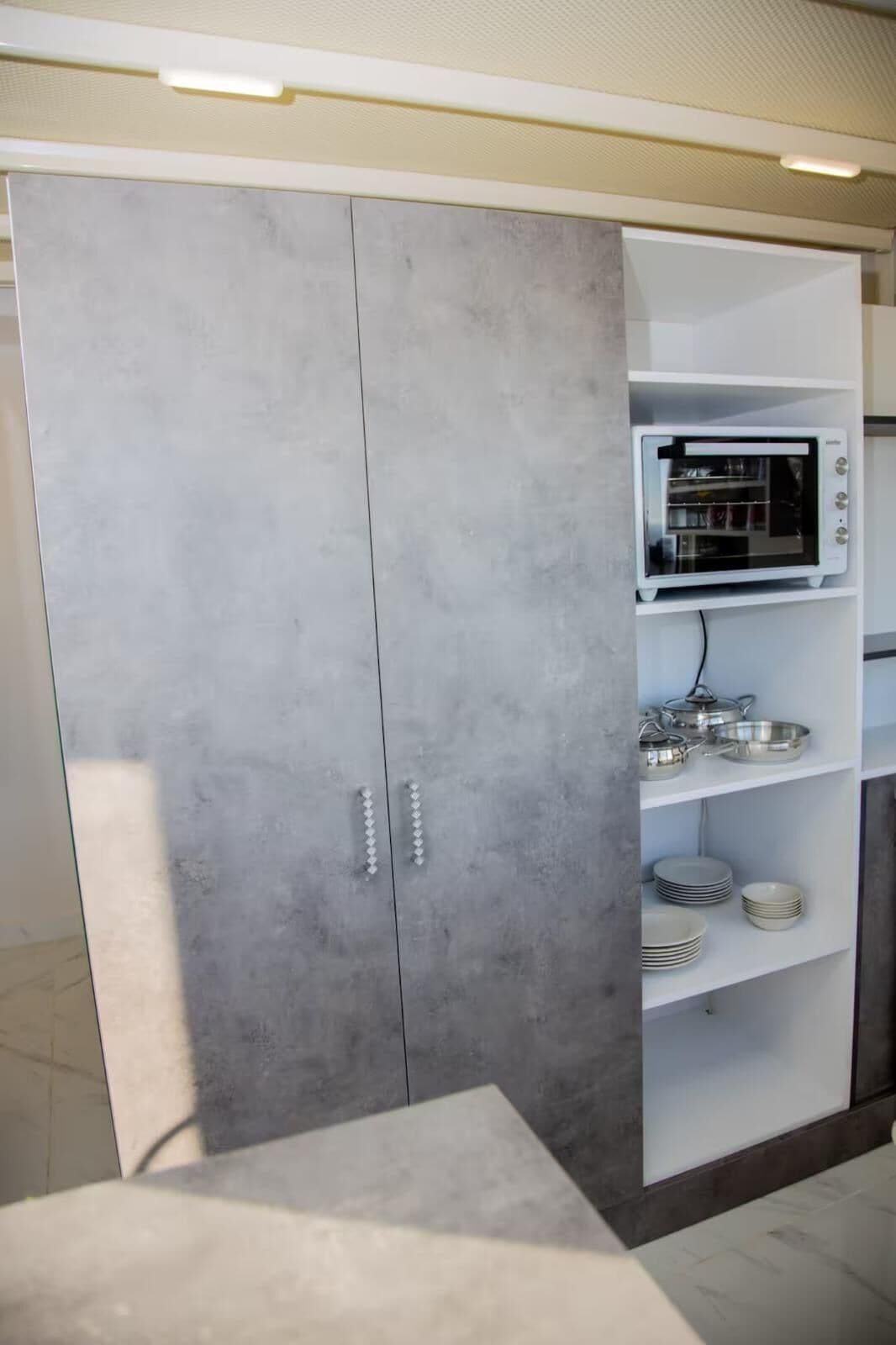 A modern kitchen with grey cabinets, a built-in oven, and a shelf with plates and bowls.