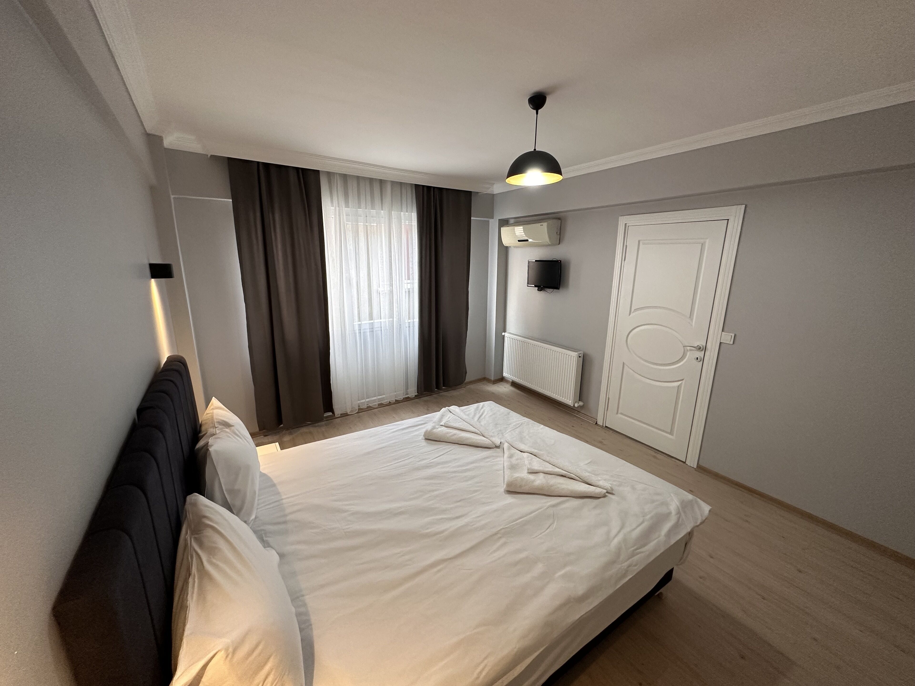 Une chambre d’hôtel avec un grand lit, une table de chevet, un téléviseur à écran plat fixé au mur, un radiateur et une porte.