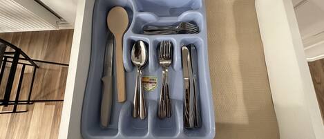 Un cajón con un organizador azul para utensilios que contiene un cuchillo, una cuchara, un tenedor y otros cubiertos.