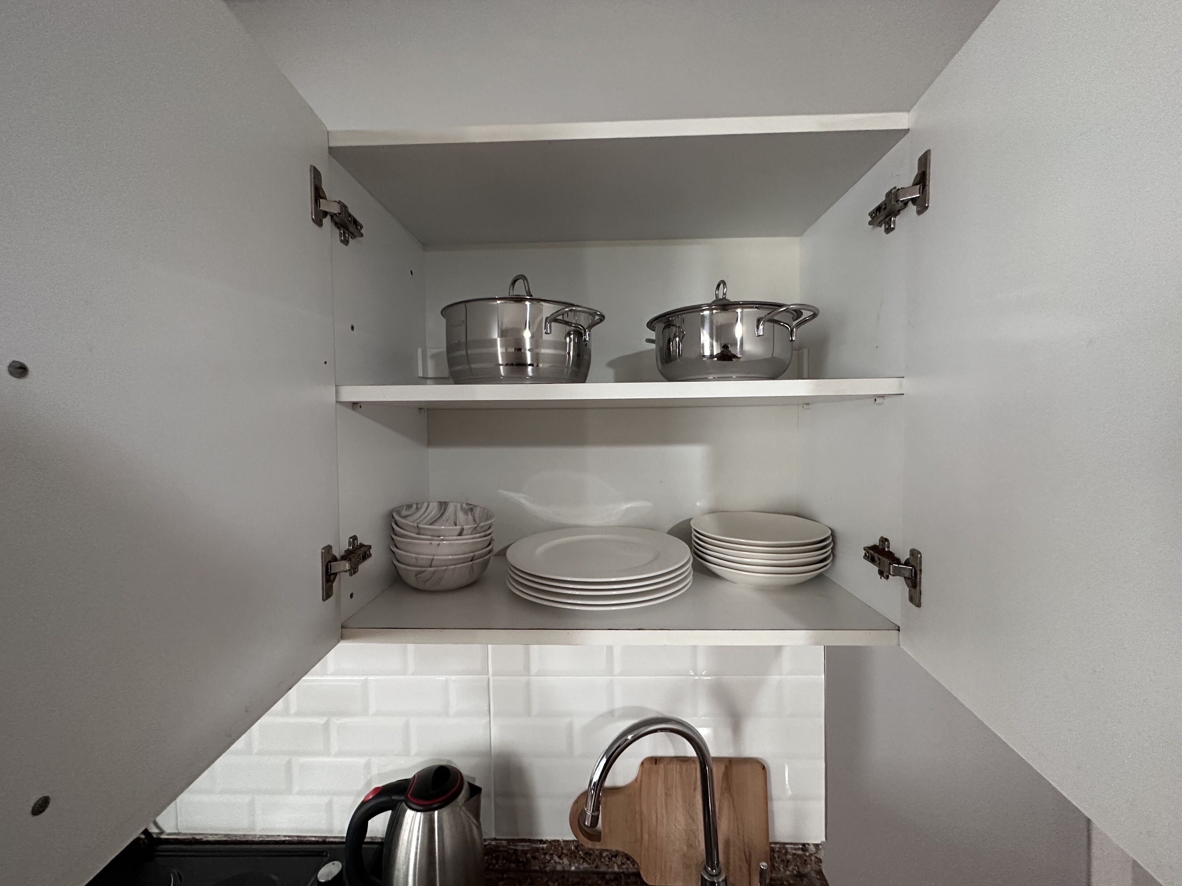 A kitchen with white cabinets, two shelves with pots and pans, and a kettle on the counter.