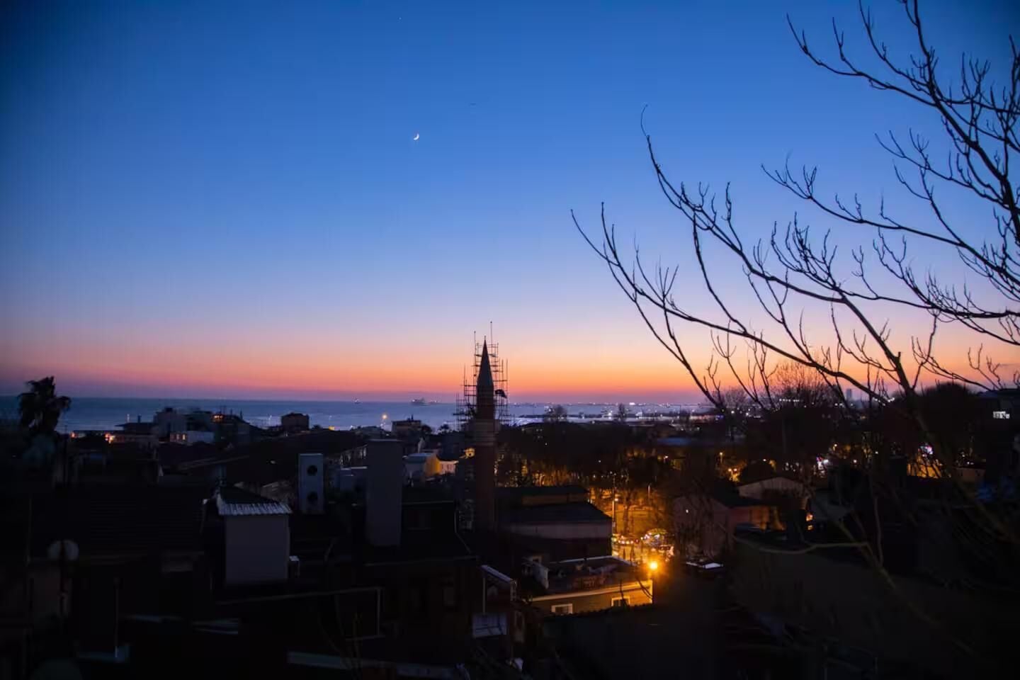 A cityscape at dusk with a prominent tower and a body of water in the background.
