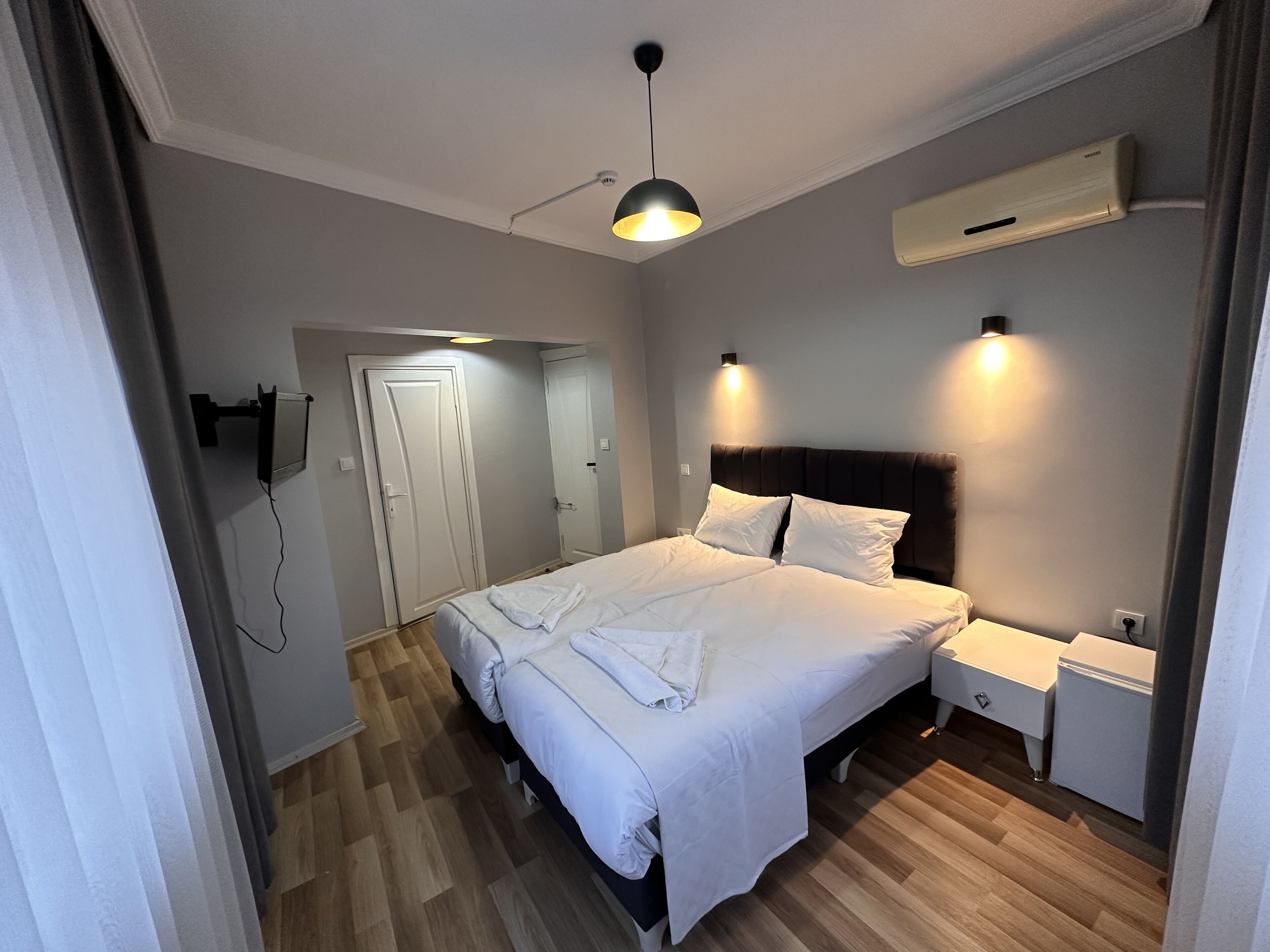 A modern bedroom with a large bed, bedside tables, a wardrobe, and an air conditioning unit.