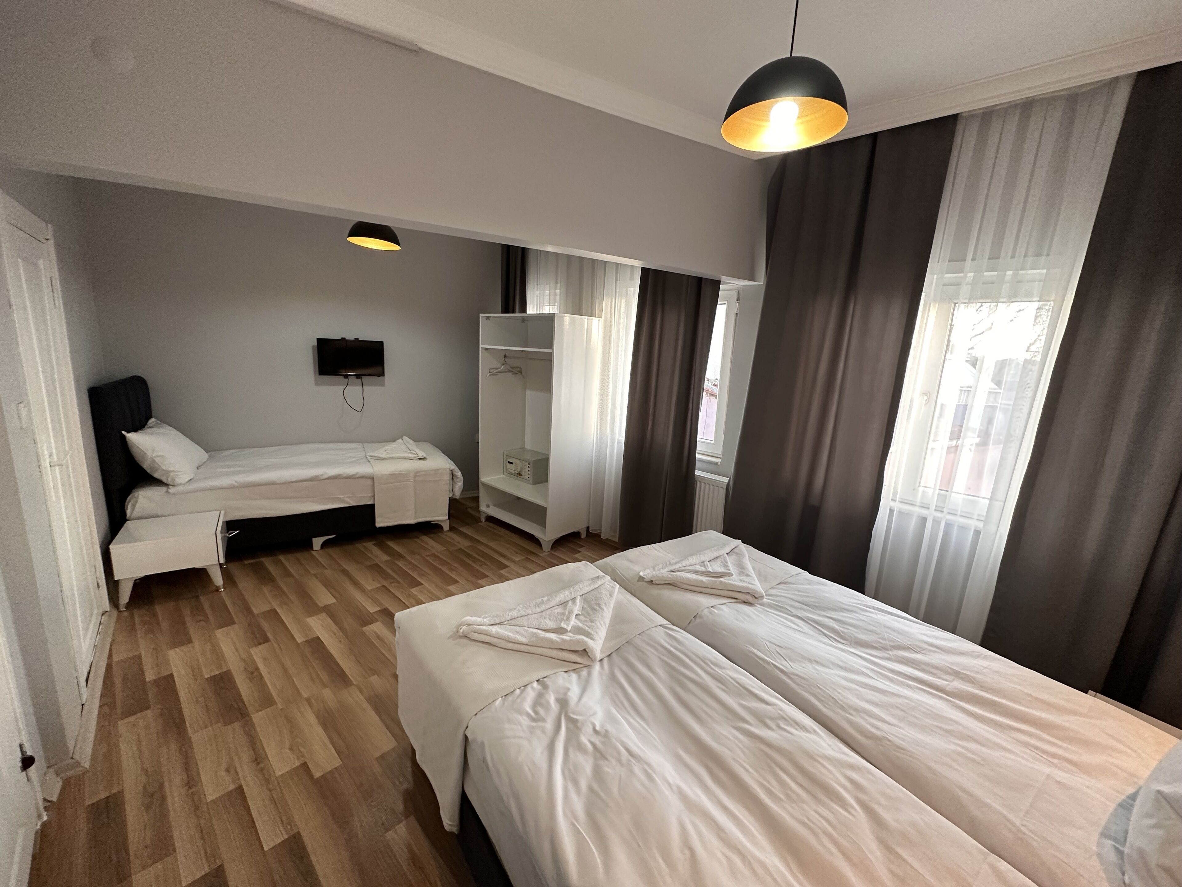 A bedroom with a bed, a wardrobe, a bedside table, a TV, and a window with curtains.