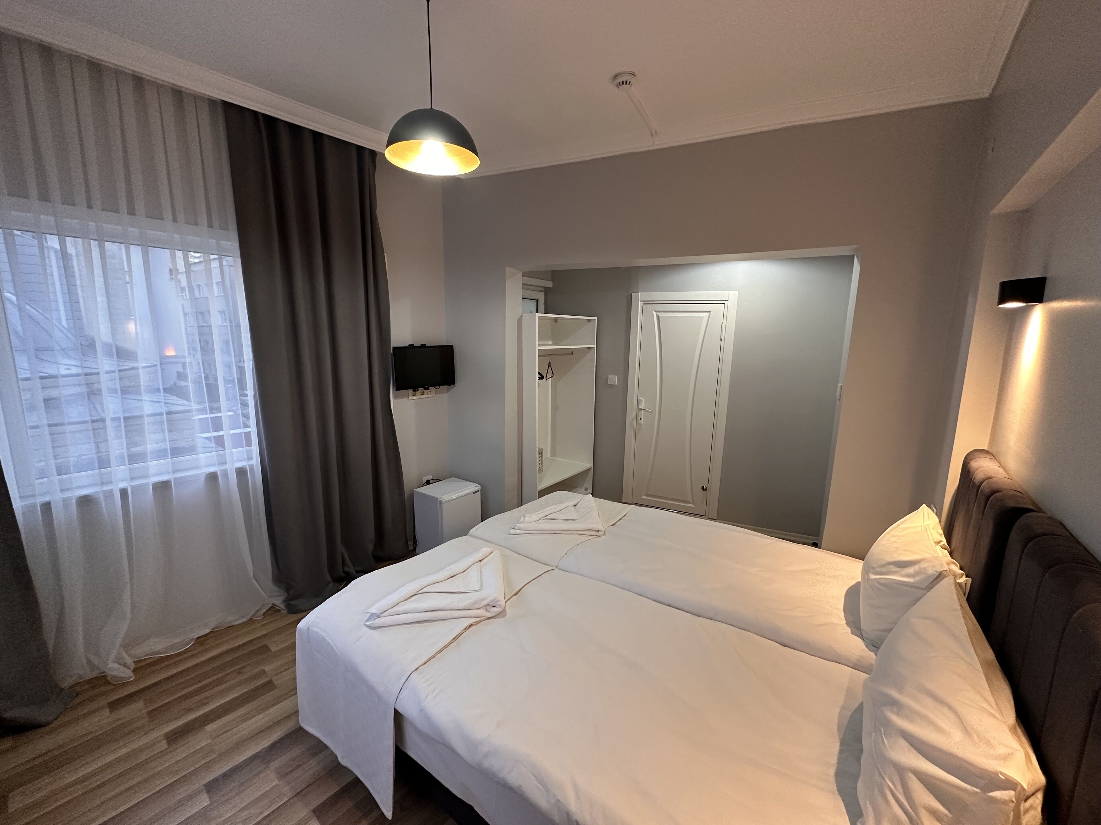 A hotel room with a bed, a TV, a wardrobe, and a window with curtains.