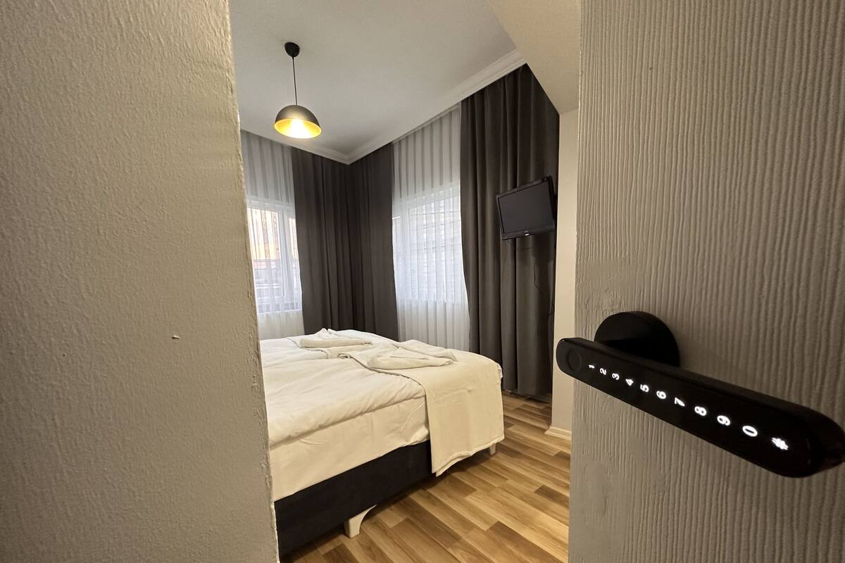A modern hotel room with a bed, a TV, and a door with a keypad lock.