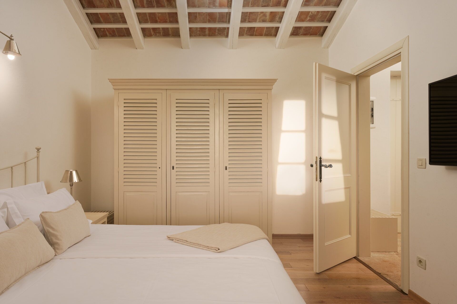 A bedroom with a bed, two wardrobes, a nightstand, a lamp, and a door leading to another room.