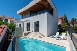 Une maison moderne à deux étages, dotée d’une piscine, d’un espace salon extérieur et d’un toit en pente en bois.