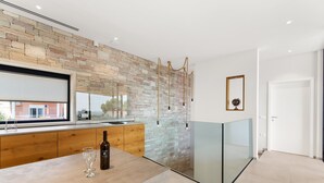 Uma cozinha moderna com painel de pedra, armários de madeira e divisória de vidro.