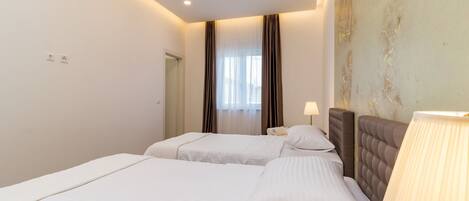 A hotel room with two beds, a bedside lamp, and a view of the outdoors through sheer curtains.