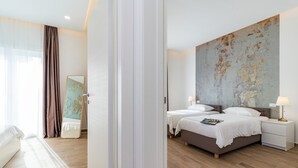 A modern hotel room with a large bed, two bedside tables with lamps, a large abstract painting on the wall, and a view of the city through the window. - Villa Lotus with Heated Pool (Pula)