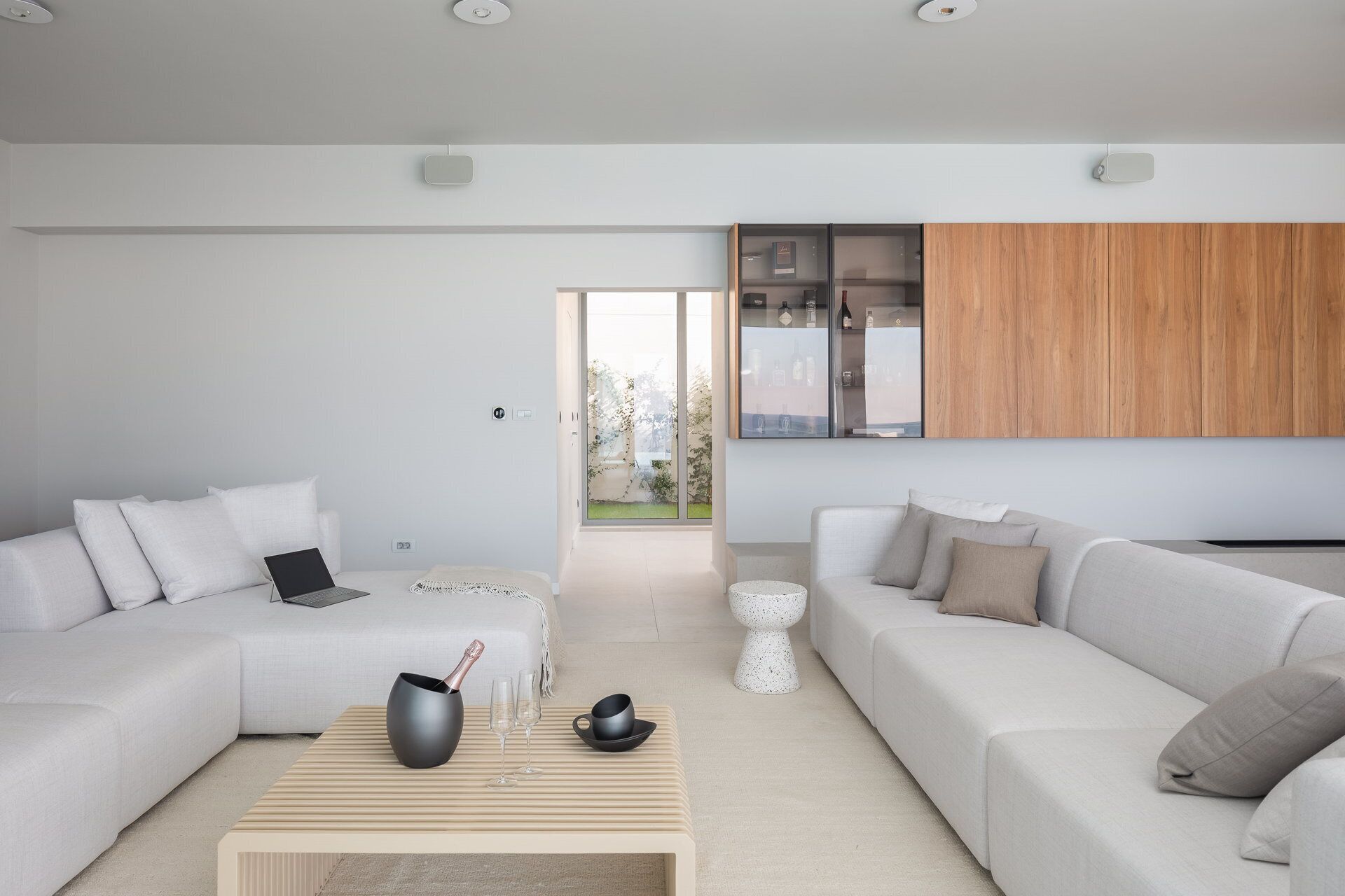 Uma sala de estar moderna com dois sofás, uma mesa de centro e uma área de cozinha com armários de madeira e uma porta de vidro.