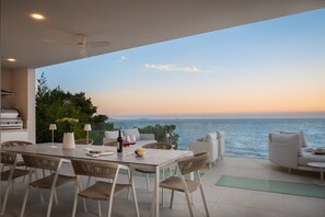 A modern outdoor dining area with a view of the sea, a grill, and comfortable seating.