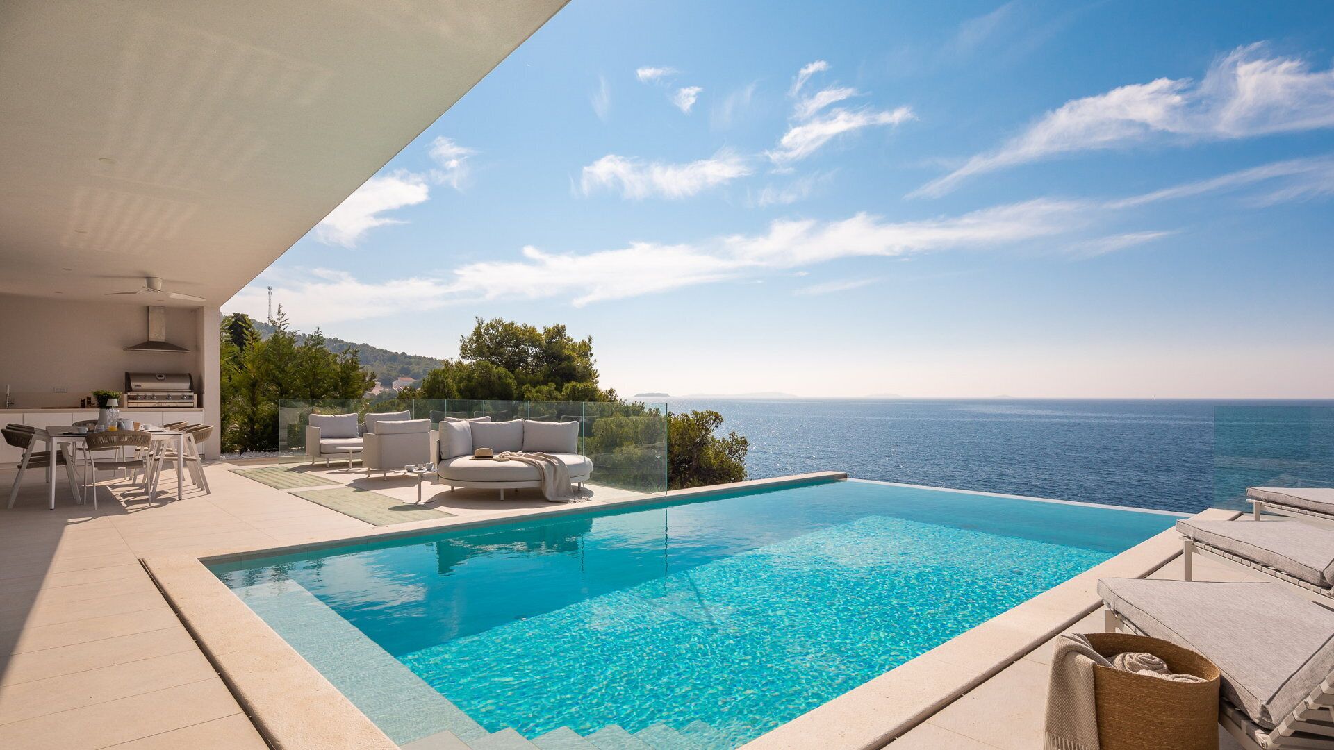 A poolside area with a view of the sea, outdoor furniture, and a barbecue setup.