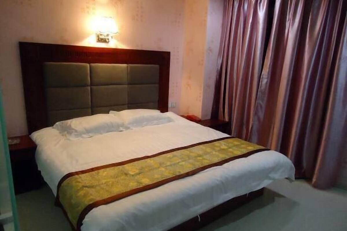 A hotel room with a bed, a nightstand, a wall-mounted light, and curtains.