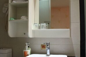 A bathroom with a white sink, a mirror above it, and a shelf with toiletries. - 168 Business Hotel (Jinjiang)