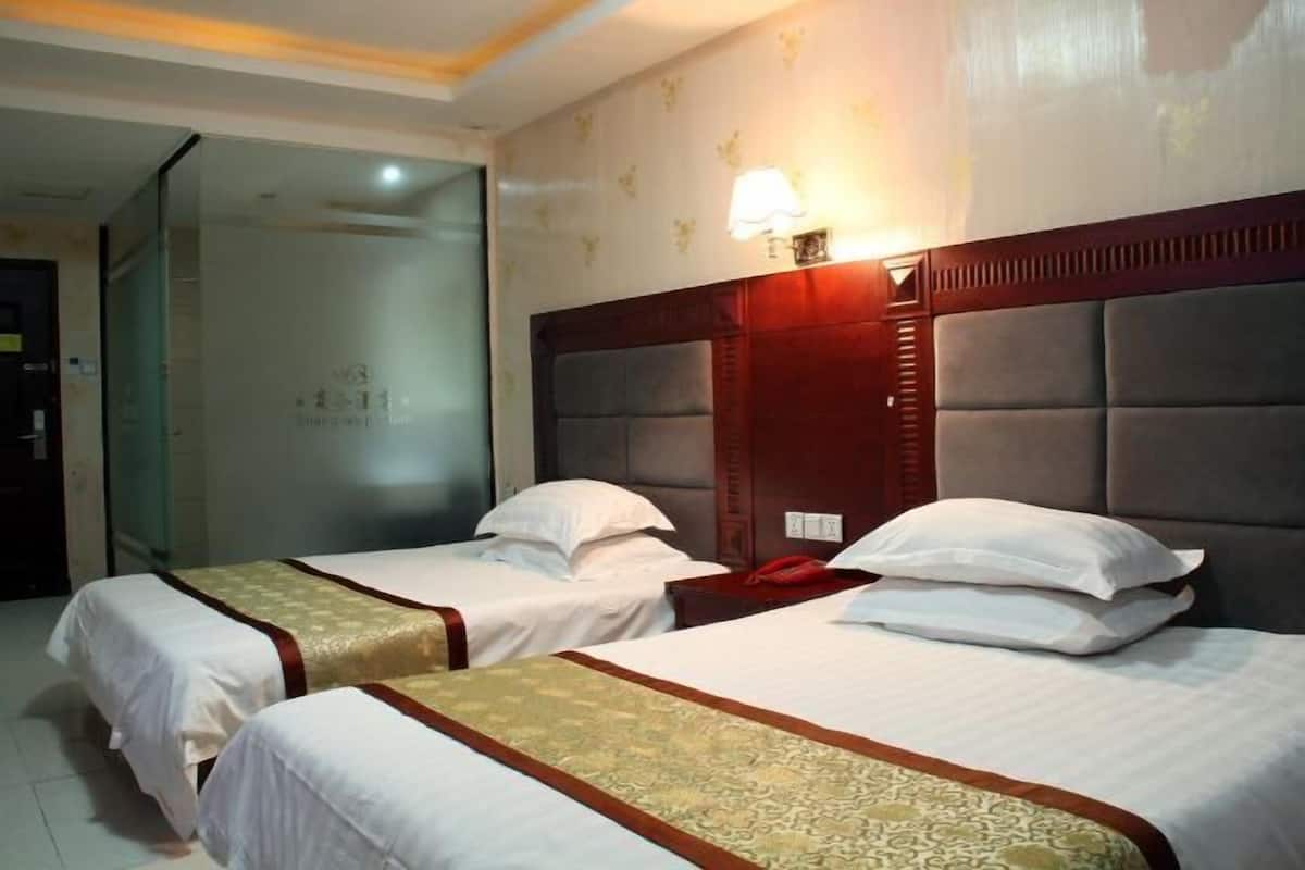 A hotel room with two single beds, a wooden headboard, a bedside table with a lamp, and a glass partition wall.