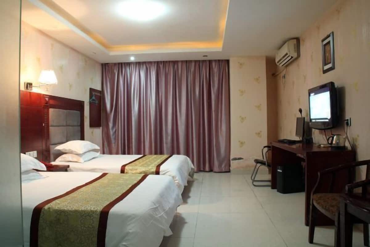 A hotel room with two beds, a desk with a computer, a chair, a television, and an air conditioning unit.