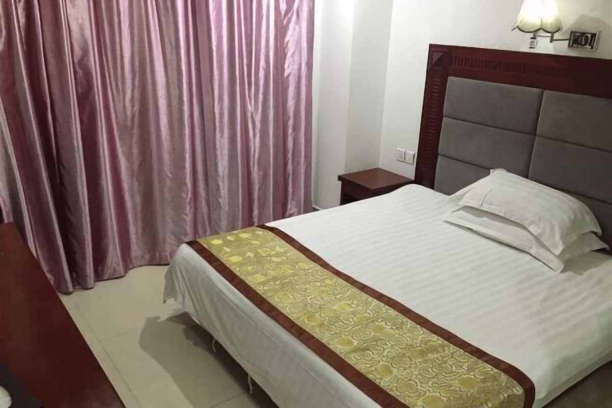 A hotel room with a bed, a nightstand, a lamp, and a curtain.