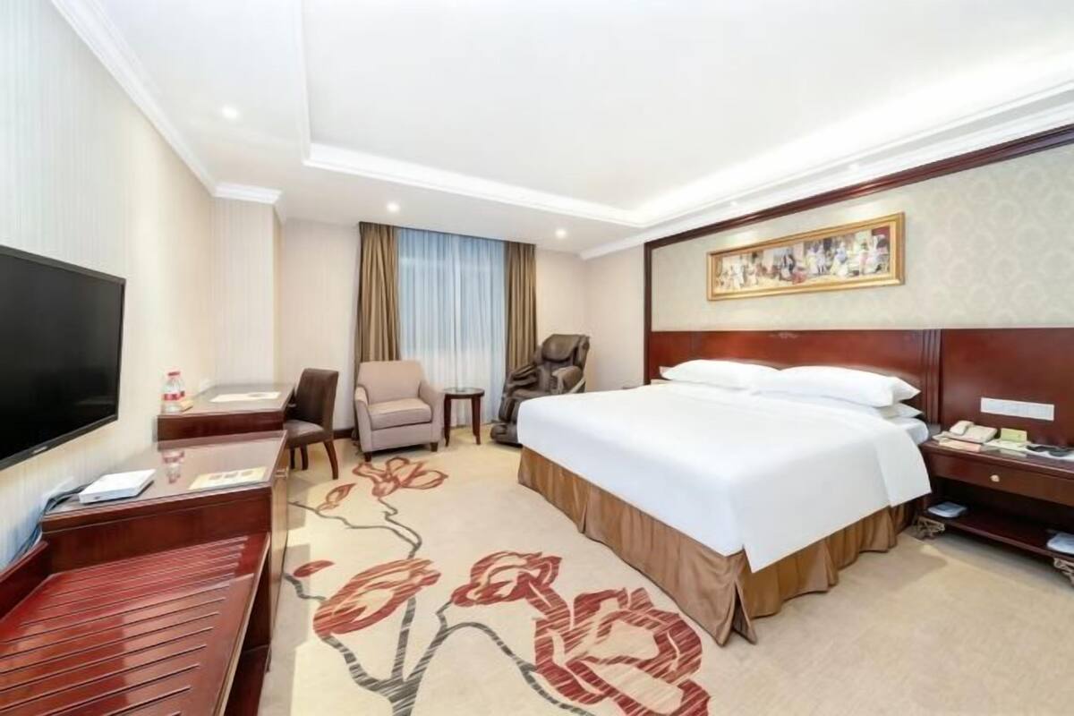 A hotel room with a bed, a TV, a desk, a chair, and a carpet.