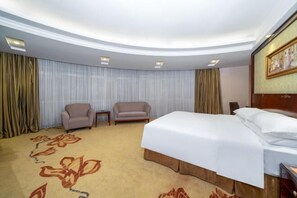 Ein Hotelzimmer mit einem großen Bett, zwei Sesseln, einem kleinen Tisch und einer Deckenleuchte.