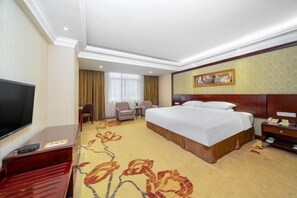 Ein Hotelzimmer mit einem großen Bett, einem Fernseher, einem Schreibtisch und einem Sessel.