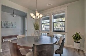 A dining area with a round table, chairs, a chandelier, and potted plants.