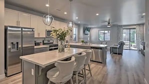 Una cocina moderna con electrodomésticos de acero inoxidable, una isla central con taburetes de bar, iluminación colgante y vistas al área de estar.