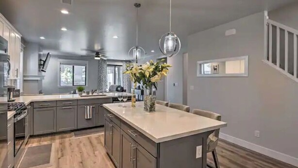 Una cocina moderna con armarios grises, una isla grande, luces colgantes y piso de madera.