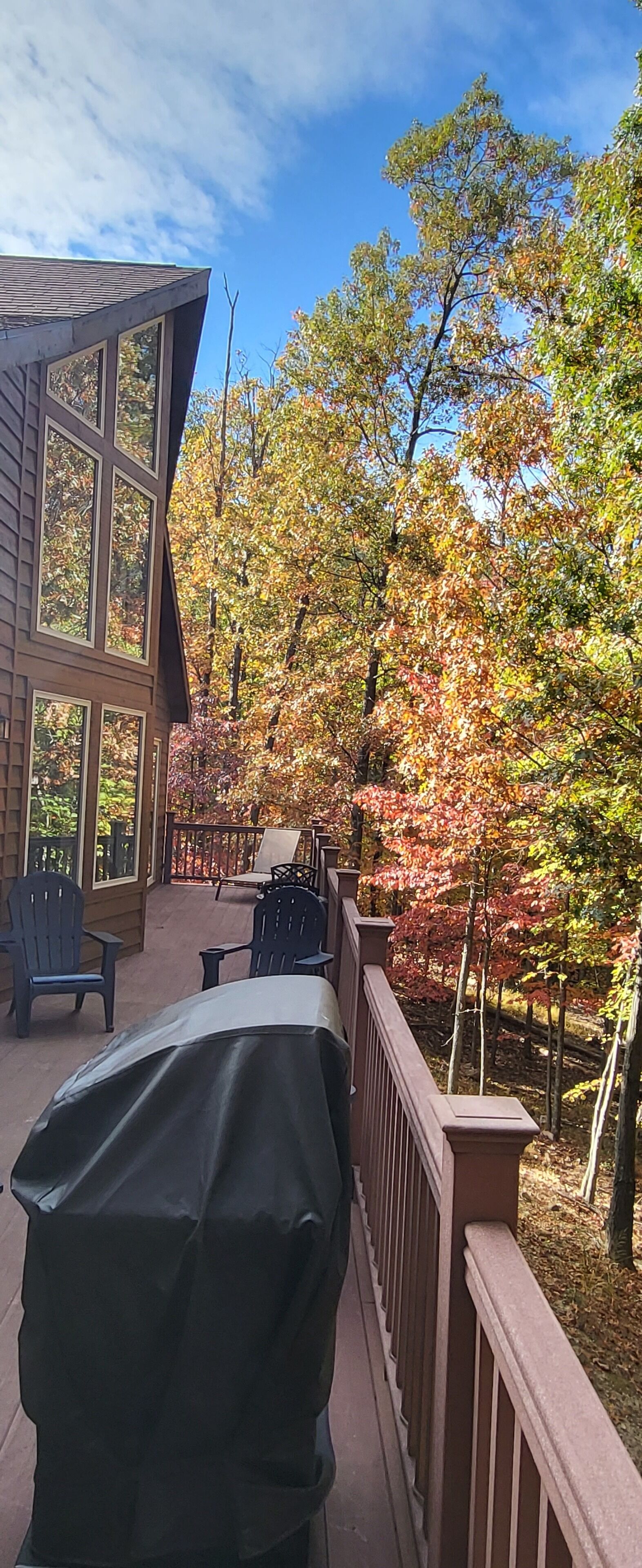 A covered outdoor deck with a barbecue grill, chairs, and a view of autumn foliage.