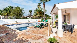 A swimming pool with lounge chairs, a covered patio area, and palm trees. - Casa Celina (Guia)