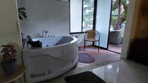 Un baño con una bañera grande, una planta en maceta y una silla cerca de un ventanal corredera.