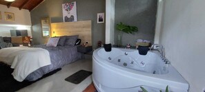 Una camera da letto con un letto grande, un'area salotto con un divano e una vasca da bagno bianca dotata di numerosi rubinetti.
