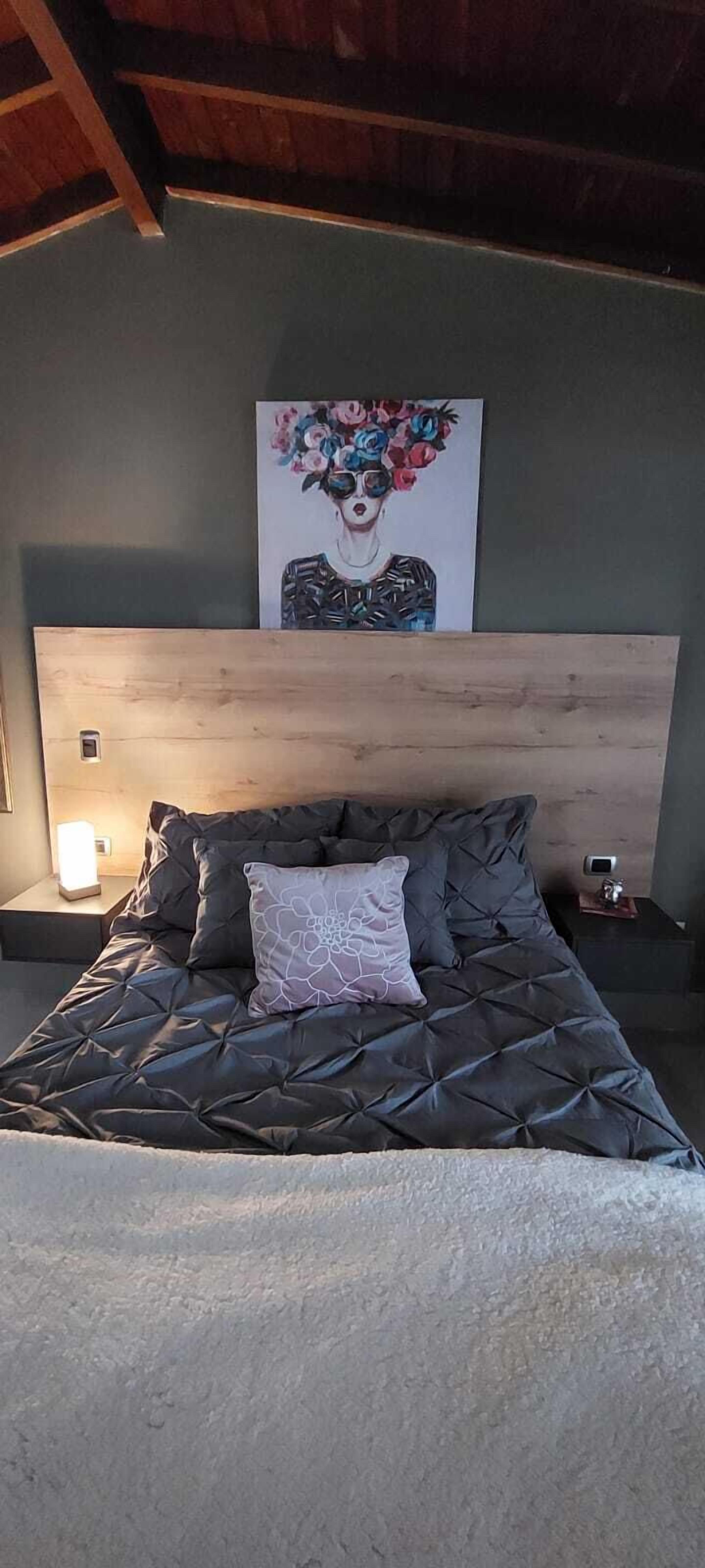 A bedroom with a large bed, a wooden headboard, a nightstand, and a wall-mounted artwork.
