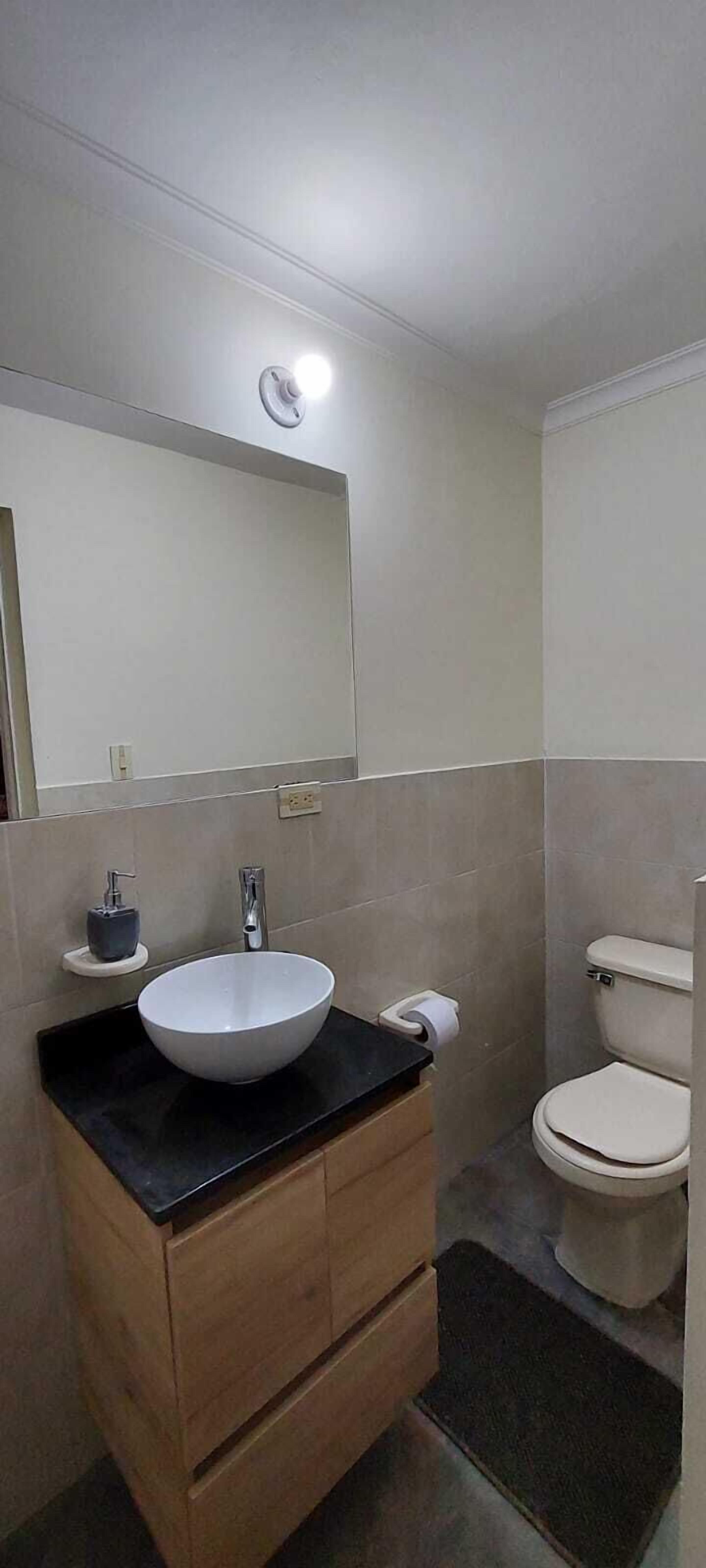 Un baño con un lavamanos blanco, un inodoro y un espejo sobre el lavamanos.