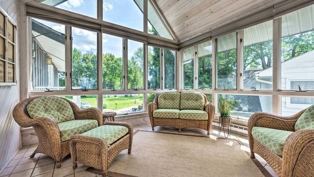A sunroom with wicker furniture and large windows overlooking a green landscape. - Large Lake House: Expansive View (Paw Paw)