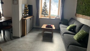 A living room with a dark grey sofa, a wooden coffee table, a small wooden desk with a TV, a Christmas tree, and a window with curtains. - House with wellness near ski slopes (Jesenice)