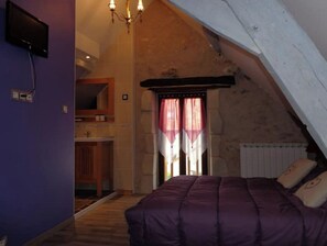 Un dormitorio con techo inclinado, cama con cubrecama púrpura, cómoda de madera, espejo y ventana con cortinas rosas.