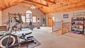Uma academia espaçosa com diversos equipamentos de exercício, uma grande janela e teto de madeira.