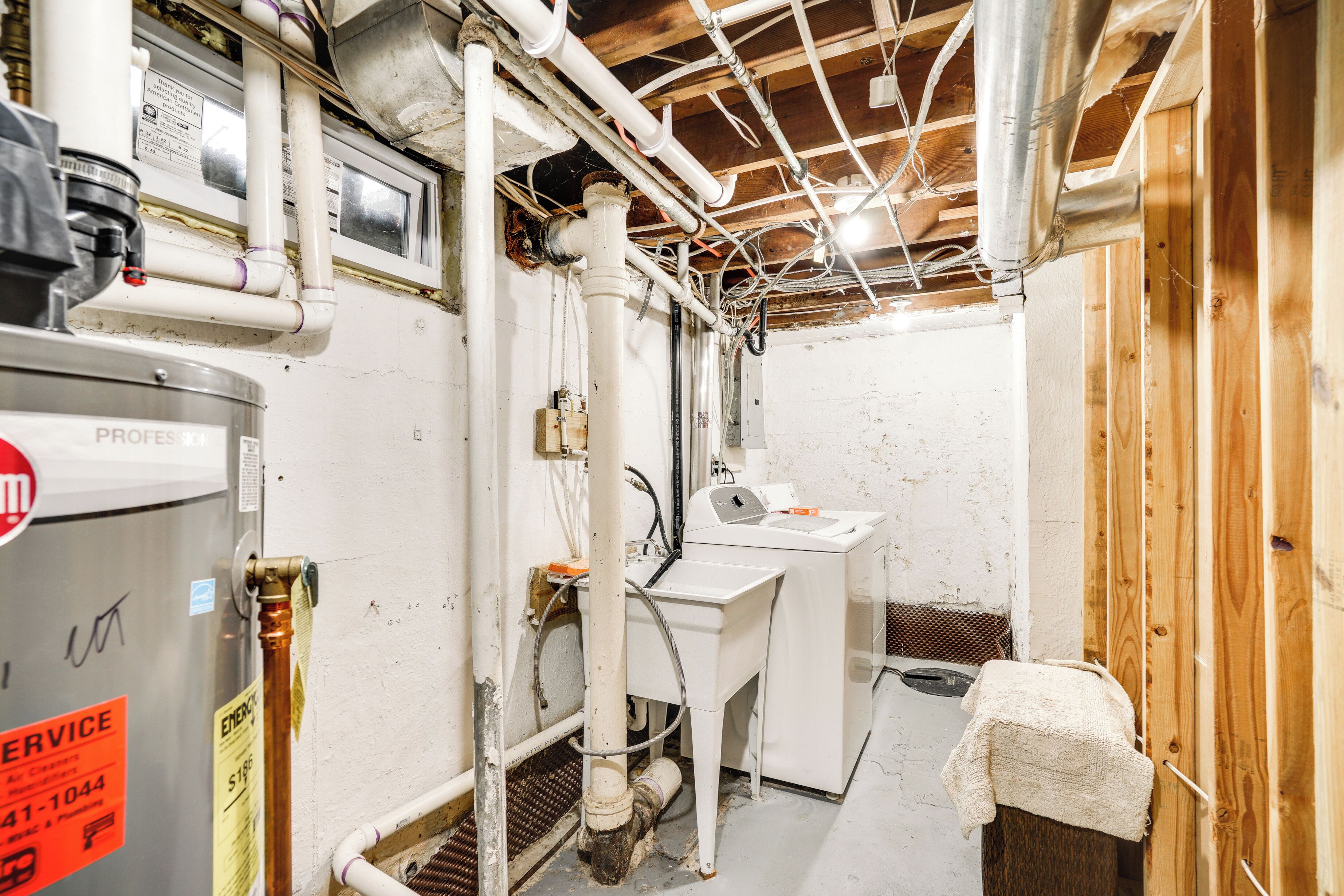 A utility room with exposed pipes, a water heater, and a sink.